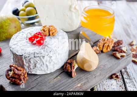 Verschiedene Käsesorten auf einem Holzbrett und viele Snacks, Nüsse, Honig, Beeren, Oliven auf einem weißen alten Holztisch. Lebensmittelzutaten zurück Stockfoto