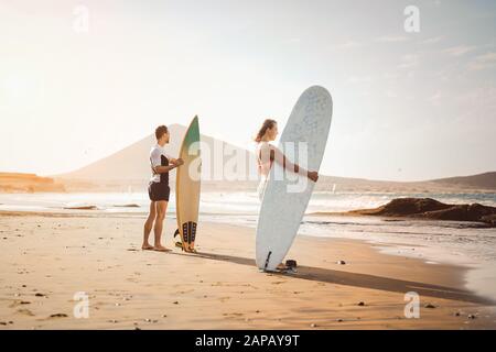 Surferpaare stehen am Strand mit Surfbrettern, die sich zum Surfen auf hohen Wellen vorbereiten - Junge Leute haben Spaß am Surftag Stockfoto