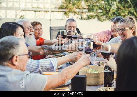 Fröhliche Familie jubelt beim Reunion-Dinner im Garten mit Rotwein - Senior hat Spaß beim Brillen und beim gemeinsamen Abendessen im Freien Stockfoto