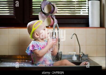 Baby spritzt in der Küchenspüle und hat Spaß mit Wasser Stockfoto