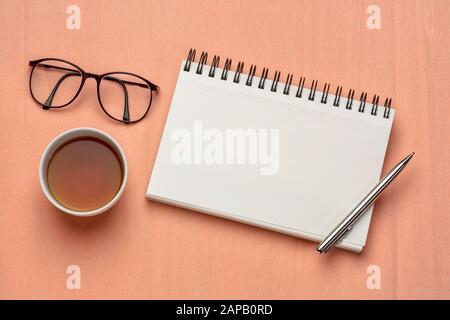 Arbeitsfläche flach mit leerem Spiralnotizbuch, Stift, Tee und Lesebrille gegen strukturiertes Papier Stockfoto