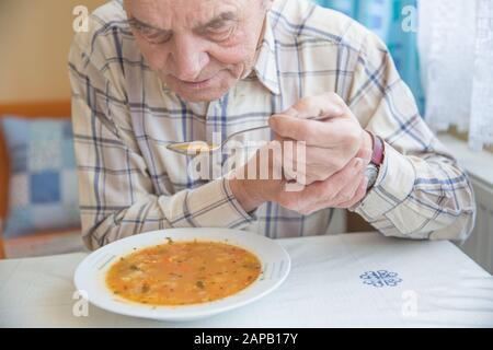Älterer Mann mit Parkinsons Krankheit hält Löffel in beiden Händen. Stockfoto