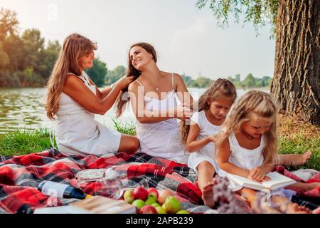 Mutter, Großmutter und Kinder weben Zöpfe miteinander. Die Familie hat Spaß beim Picknick im Park. Frauentag Stockfoto