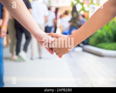 Die Eltern oder Mutter, die ein Handkind auf der Straße zum Einkaufszentrum in der Stadt mit Glück spazieren hält. Das Konzept der Haltehand. Stockfoto