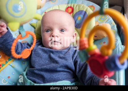 Authentisches Bild eines süßen Jungen im Alter von fünf Monaten in einem Aktivitätsstuhl, der Interesse an interessanten hängenden Spielzeugen hat. England, Großbritannien, Großbritannien Stockfoto