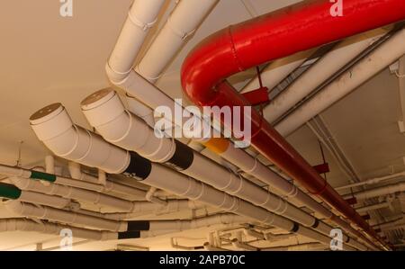 Nahgruppe von Wasserleitungen, die an der Decke eines Gebäudes hängen, selektiver Fokus, die rote Leitung ist für die Brandbekämpfung vorgesehen Stockfoto