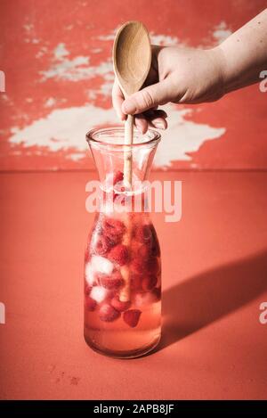 Herstellen von Himbeeren Limonade mit Eiswürfeln, tonischem Wasser und gefrorener Himbeere auf einem üppigen Lavafisch. Frau, die ein Himbeergetränk mischt. Kaltes Sommergetränk. Stockfoto