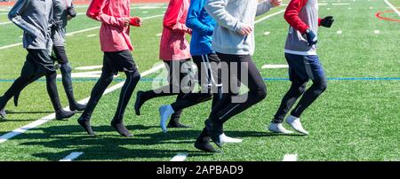 High-School-Jungen ziehen an einem sonnigen, aber kalten Winternachmittag ihre Schuhe aus und joggen auf dem Rasen in ihren Socken. Stockfoto