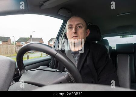 Ein Mann mittleren Alters saß hinter einem Lenkrad auf dem Fahrersitz eines Autos. Stockfoto