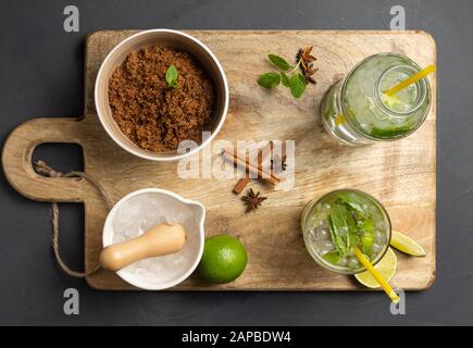 Caipirinha, Limette, frische Minze, brauner Zucker und zerkleinertes Eis. Rustikale Umgebung mit schwarzem Hintergrund. Luftansicht Stockfoto