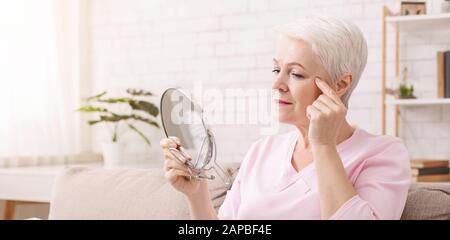 Seniorin untersucht ihre Gesichtshaut auf Falten Stockfoto