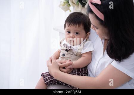 Der Babyjunge sitzt auf dem Schoß seiner Mutter Stockfoto
