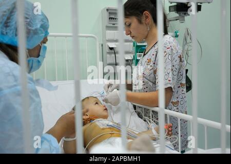 Auf der Intensivstation. Krankenschwester steht in der Nähe eines Krankenhausbetts, wobei das Baby es für die Behandlung vorbereitet. Children'S Cardiac Center. Mai 18,2018. Kiew, Ukraine Stockfoto