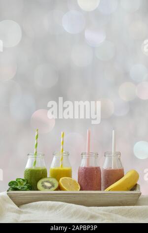 Vier bunte Fruchtsmoothies in einer Reihe mit frischen Früchten vor neutralem, hellem, unscharfem Bokeh-Hintergrund mit kopierbarer Fläche oben für ein gesundes Lifestyl Stockfoto