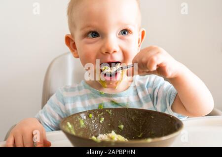 Kleiner Junge allein isst Püree aus einer Platte. Stockfoto