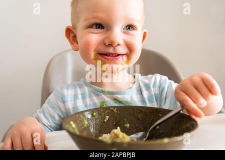 Kleiner Junge allein isst Püree aus einer Platte. Stockfoto