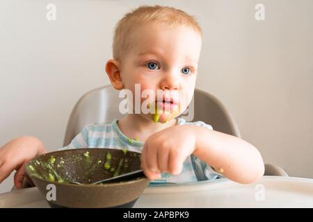 Kleiner Junge allein isst Püree aus einer Platte. Stockfoto