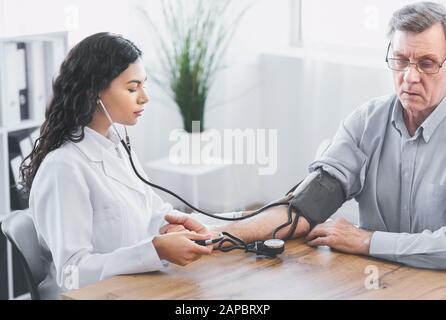 Weiblicher Arzt überprüft den Blutdruck des reifen Mannes Stockfoto