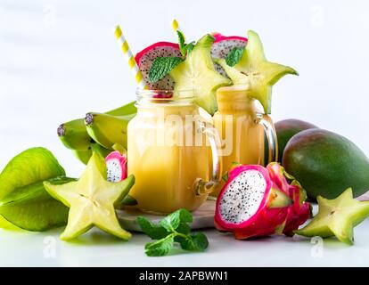 Eine Nahaufnahme von zwei tropischen exotischen Fruchtsmoothies in Glasgefäßen, umgeben von exotischen tropischen Früchten. Stockfoto