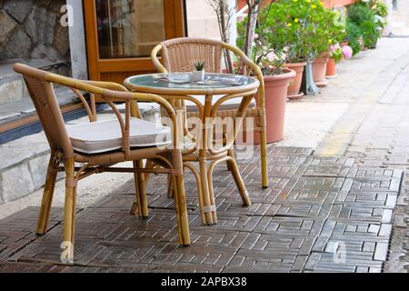 Rattan-Tisch und -Stühle im Freien Sommerveranda des Kaffeehauses. Blumentöpfe mit grünen Pflanzen im Hintergrund. Stockfoto