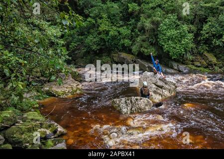 Wanderer, die den Oparara Arch, am Felsbrocken am Oparara River, Regenwald, Kahurangi National Park, West Coast Region, South Island, Neuseeland betrachten Stockfoto