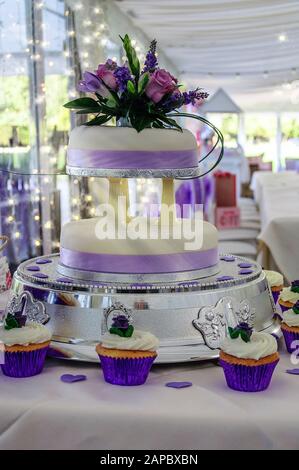 Blasslila und weißer Hochzeitstorte auf einem Tisch mit Cupcakes. Stockfoto