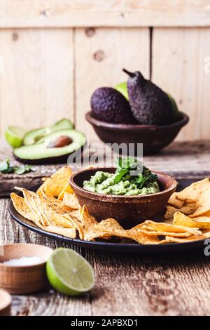 Mexikanische traditionelle Küche, Guacamolesauce, Zutaten Avocado, Cilantro, Limetten- und Tortilla-Maisspäne auf ländlichem Holztisch. Lokale Küche wird vorbereitet Stockfoto