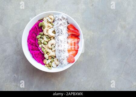 Gesundes Frühstück Smoothie-Schüssel mit Pitaya, Cashew, Kokosflocken und Erdbeere auf grauem Hintergrund. Kopierbereich. Stockfoto