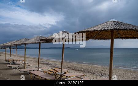 Winterzeit am Strand. Strohschirme und liegen in Reihe an einem sandigen, leeren Strand. Flauschige dunkle Wolken und ein Boot inmitten einer ruhigen blauen se Stockfoto