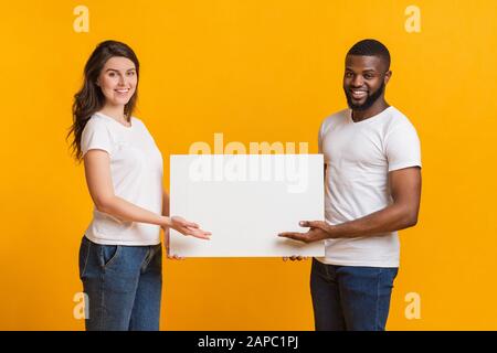 Junge Frau und afro-Mann halten und zeigen auf ein leeres Schild Stockfoto