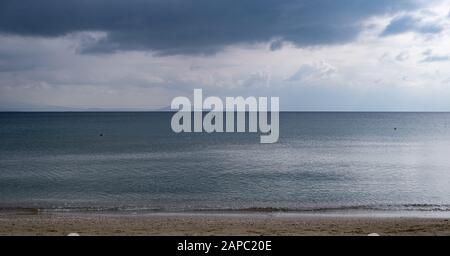 Flauschige graublaue Wolken treffen auf ruhiges dunkelblaues Meer weit von der sandigen Küste entfernt. Orangefarbene Bojen und ein Boot mitten im Meer. Hintergrund der Berge, Spac Stockfoto