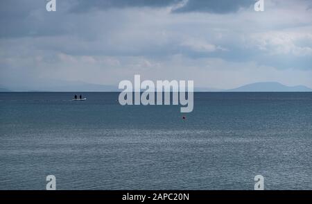 Flauschige graue Wolken treffen auf ruhiges dunkelblaues Meer. Eine orangefarbene Boje und ein Boot mitten im Meer. Berge Hintergrund, Raum. Stockfoto