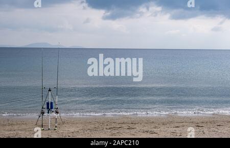 Zwei Angelruten steckten richtig in einen leeren sandigen Strand, der auf einen Fisch wartete. Flauschige dunkelblaue Wolken Hintergrund, Raum. Stockfoto