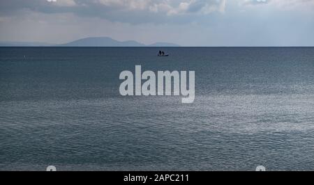 Flauschige graue Wolken treffen auf ruhiges dunkelblaues Meer. Ein Boot mitten im Meer. Berge Hintergrund, Raum. Stockfoto