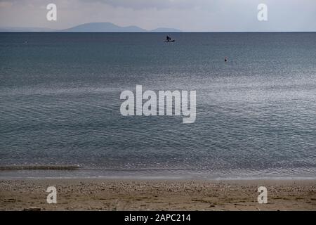 Flauschige graublaue Wolken treffen auf ruhiges dunkelblaues Meer weit von der sandigen Küste entfernt. Orangefarbene Bojen und ein Boot mitten im Meer. Hintergrund der Berge, Spac Stockfoto