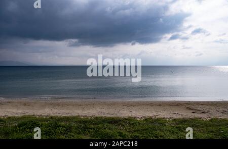 Der Hintergrund der schweren, flauschigen Wolken trifft auf ein ruhiges dunkelblaues Meer weit von der sandigen Küste entfernt. Orangefarbene Bojen und ein Boot mitten im Meer. Copyspace. Stockfoto