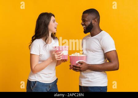 Fröhliches Interracial Paar Hält Popcorn Eimer Und Lacht Über Gelben Hintergrund Stockfoto