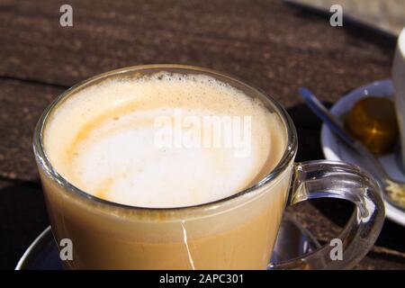 Nahaufnahme von isoliertem braunem holländischem Milchkaffee (Koffie verkeerd) in transparentem Glasbecher auf runder Holztafel Stockfoto