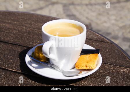 Nahaufnahme der isolierten weißen Espresso-Tasse mit Untertasse, Löffel und süßem Plätzchen auf runder Holztafel Stockfoto
