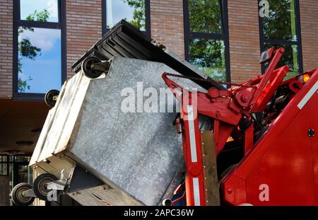 VENLO, NIEDERLANDE - 8. AUGUST. 2019: Blick auf roten Müllwagen mit hydraulischen Armen, der einen schweren Müllcontainer hebt Stockfoto