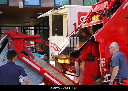 VENLO, NIEDERLANDE - 8. AUGUST. 2019: Blick auf roten Müllwagen mit hydraulischen Armen, der einen schweren Müllcontainer hebt Stockfoto