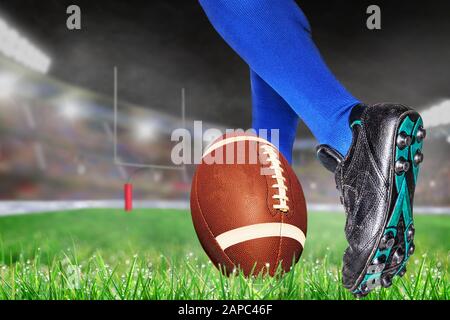 Der American Footballspieler bereitet sich darauf vor, den Ball für Konvertierungspunkte oder Field Goal im hell erleuchteten Outdoor-Stadion mit Fokus auf Vordergrund und Shallo zu treten Stockfoto