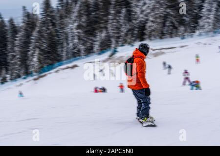 Rückansicht des nicht erkennbaren Männchens im hellen Skianzug, der sich auf dem Snowboard in Bewegung verwischt nach unten bewegt Stockfoto
