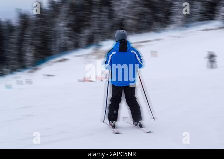 Rückansicht des nicht erkennbaren Männchens im hellen Skianzug, der sich auf dem Ski nach unten bewegt. Stockfoto