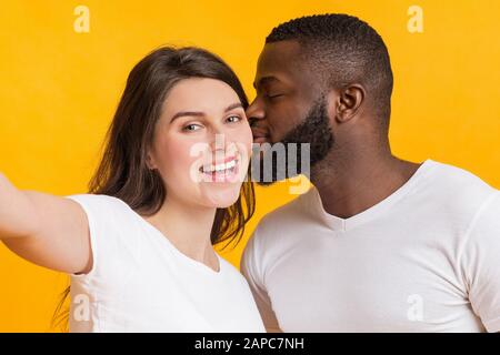 Romantisches multiracial Paar, das selfie, liebenden schwarzen Kerl nimmt, der seine Freundin küsst Stockfoto