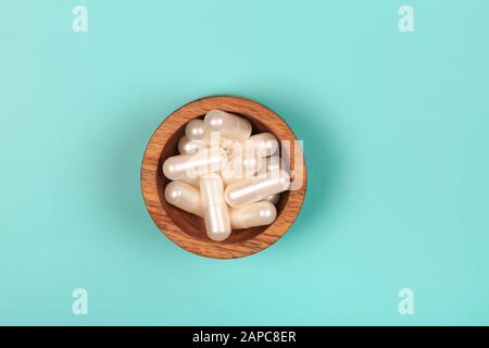 Kollagen in Kapseln in Holzschale auf pastellblauem Grund Stockfoto