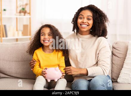 Mutter Und Tochter, Die Piggybank Auf Der Couch Zu Hause Sitzen Stockfoto