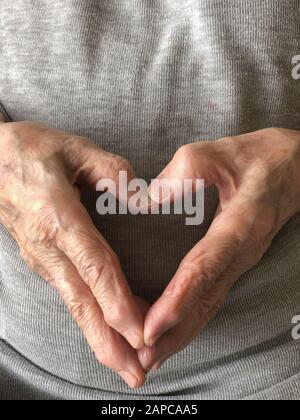 Zerknitterte Hände einer älteren Person, die Herzform mit Kopierraum macht Stockfoto