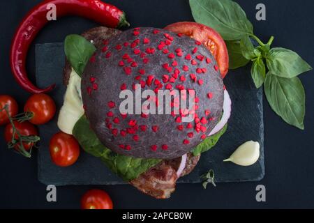 Schwarzer Hamburger und Herzen auf Steinplatte, Liebesburger Fast-Food-Konzept, Valentins-Day-Überraschungsabendessen, Holzhintergrund, Draufsicht flach lag Stockfoto