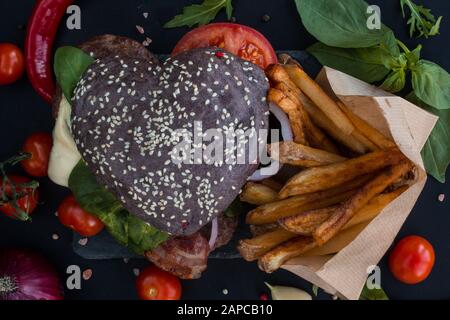 Herzförmige schwarz Hamburger und Pommes frites auf der Steinplatte, liebe Burger fast food Konzept, Valentinstag Überraschung zum Abendessen, Holz- Hintergrund, oben vi. Stockfoto